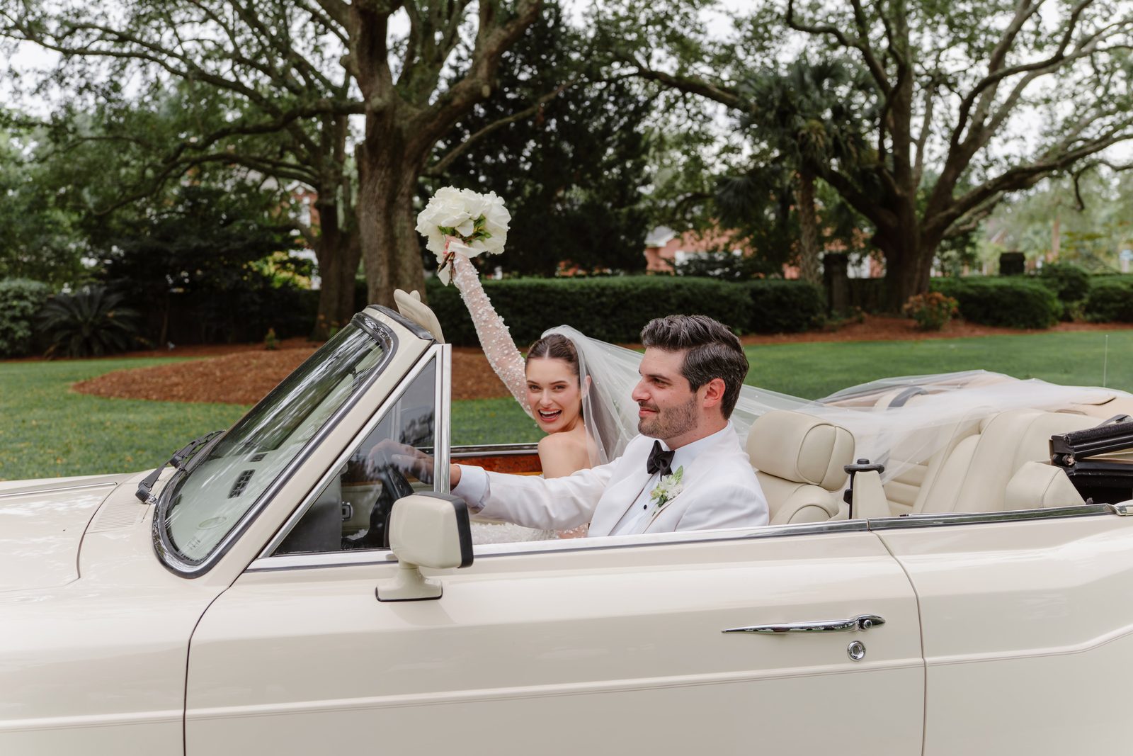Newlyweds driving off in a vintage cream convertible