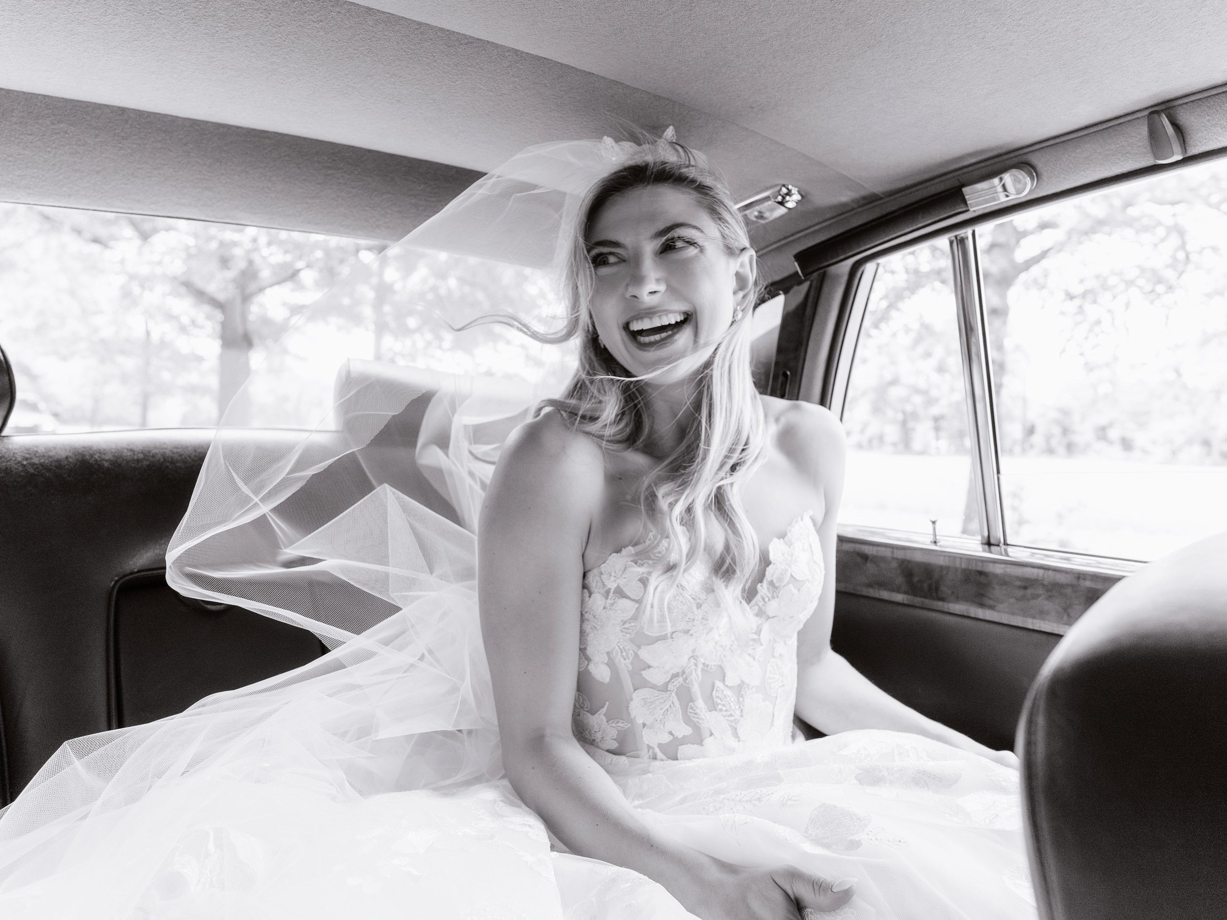 A bride laughing in the back of the vintage getaway car