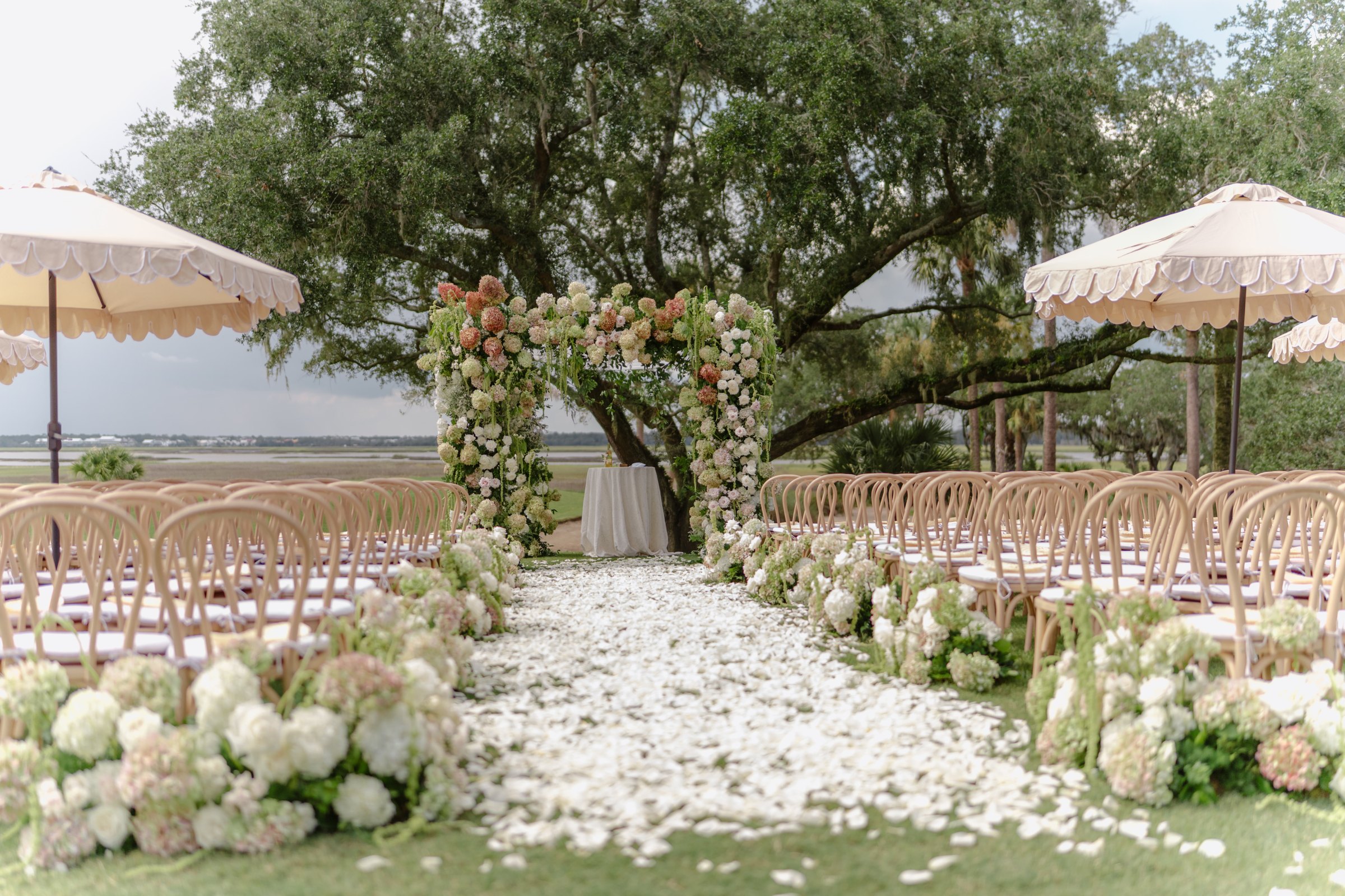 The ceremony beneath the oaks — petal aisle and marsh view