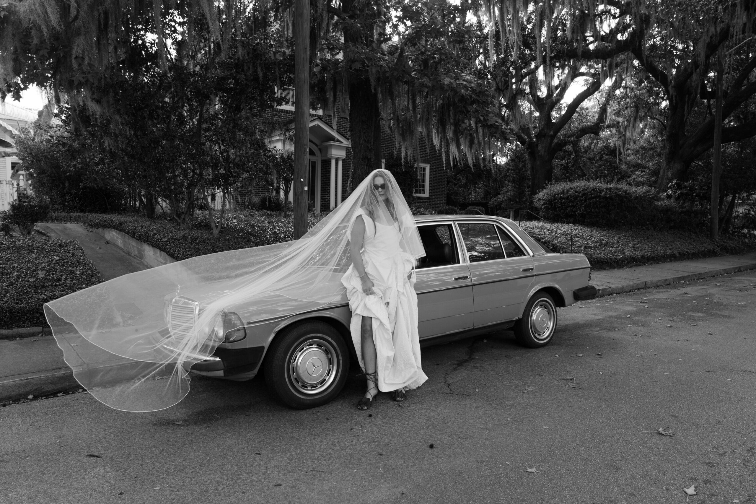 Bride in Charleston sitting on car.